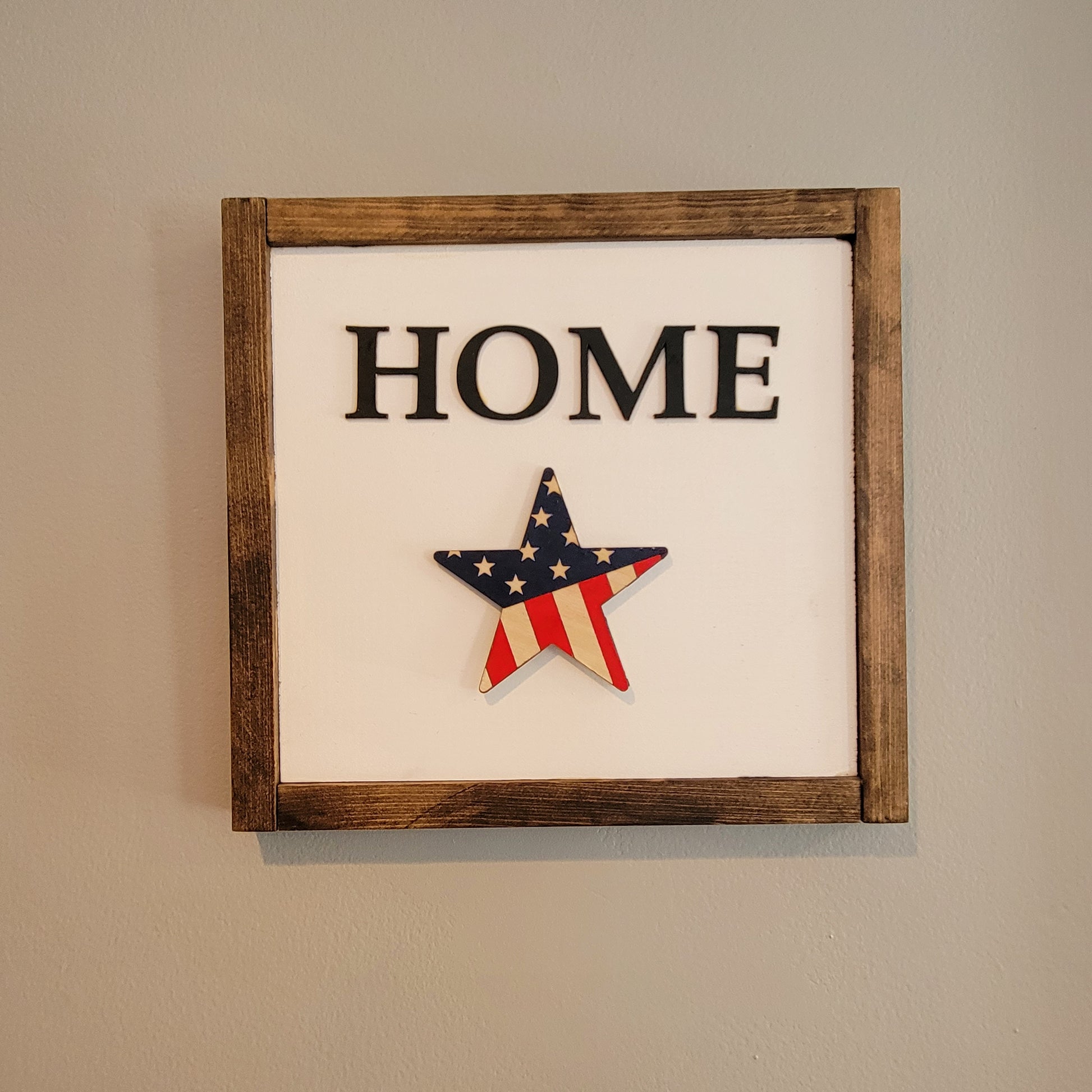 Dark wood framed home sign hanging on wall with patriotic flag star