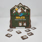 Layered wooden hiking tracker sign featuring mountains, evergreen trees, a river, and sunrise, with the text “Miles Hiked This Year” and interchangeable number tiles
